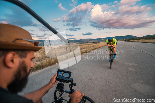 Image of A videographer recording a triathlete riding his bike preparing for an upcoming marathon.Athlete's physical endurance and the dedication required to succeed in the sport.