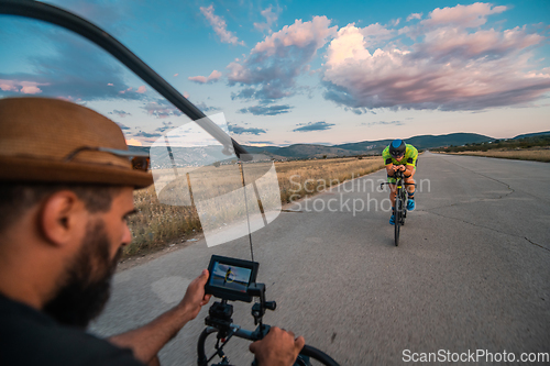 Image of A videographer recording a triathlete riding his bike preparing for an upcoming marathon.Athlete's physical endurance and the dedication required to succeed in the sport.