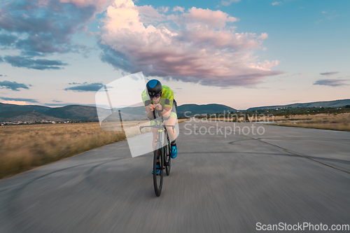 Image of Triathlete riding his bicycle during sunset, preparing for a marathon. The warm colors of the sky provide a beautiful backdrop for his determined and focused effort.