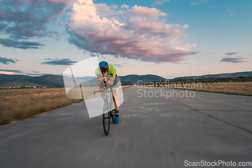 Image of Triathlete riding his bicycle during sunset, preparing for a marathon. The warm colors of the sky provide a beautiful backdrop for his determined and focused effort.