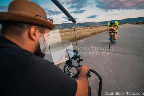 Image of A videographer recording a triathlete riding his bike preparing for an upcoming marathon.Athlete's physical endurance and the dedication required to succeed in the sport.