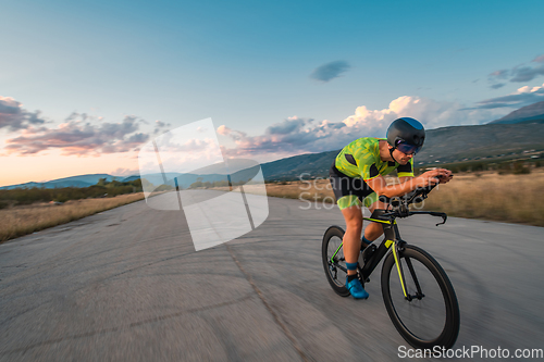 Image of Triathlete riding his bicycle during sunset, preparing for a marathon. The warm colors of the sky provide a beautiful backdrop for his determined and focused effort.