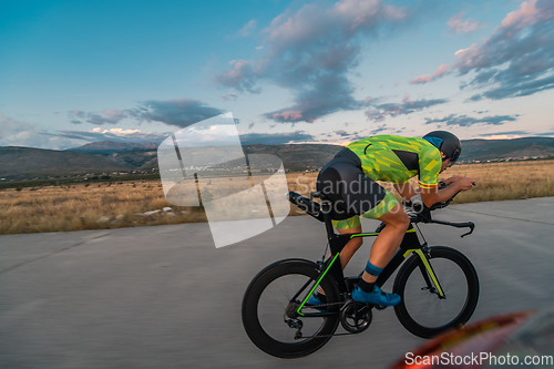 Image of Triathlete riding his bicycle during sunset, preparing for a marathon. The warm colors of the sky provide a beautiful backdrop for his determined and focused effort.