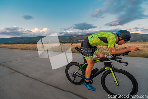 Image of Triathlete riding his bicycle during sunset, preparing for a marathon. The warm colors of the sky provide a beautiful backdrop for his determined and focused effort.