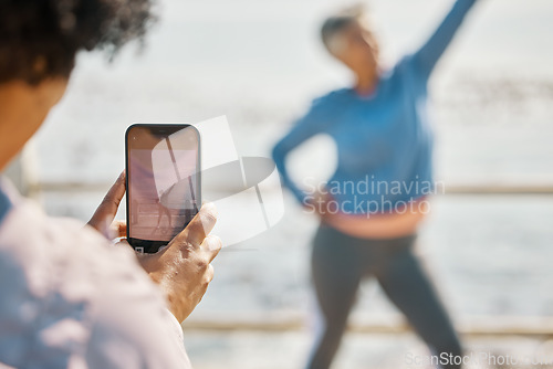 Image of Phone, fitness and photograph of woman at beach in silly pose at sea for senior friends. Exercise, mobile and picture for social media post on a ocean promenade walk for nature workout and friendship