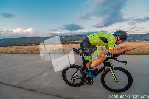 Image of Triathlete riding his bicycle during sunset, preparing for a marathon. The warm colors of the sky provide a beautiful backdrop for his determined and focused effort.