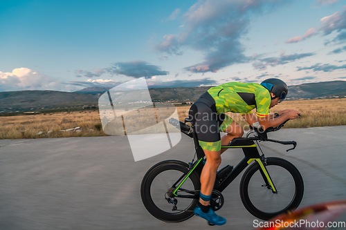 Image of Triathlete riding his bicycle during sunset, preparing for a marathon. The warm colors of the sky provide a beautiful backdrop for his determined and focused effort.