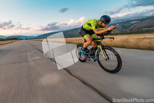 Image of Triathlete riding his bicycle during sunset, preparing for a marathon. The warm colors of the sky provide a beautiful backdrop for his determined and focused effort.