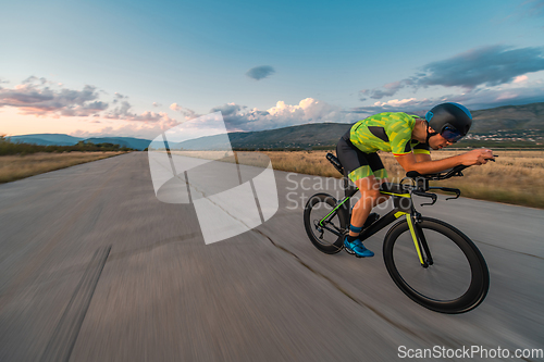 Image of Triathlete riding his bicycle during sunset, preparing for a marathon. The warm colors of the sky provide a beautiful backdrop for his determined and focused effort.