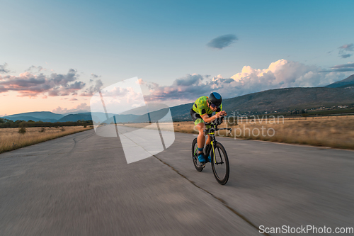 Image of Triathlete riding his bicycle during sunset, preparing for a marathon. The warm colors of the sky provide a beautiful backdrop for his determined and focused effort.