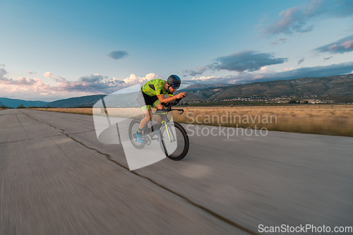 Image of Triathlete riding his bicycle during sunset, preparing for a marathon. The warm colors of the sky provide a beautiful backdrop for his determined and focused effort.