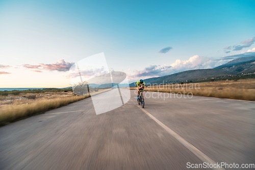 Image of Triathlete riding his bicycle during sunset, preparing for a marathon. The warm colors of the sky provide a beautiful backdrop for his determined and focused effort.