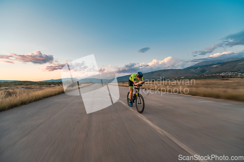 Image of Triathlete riding his bicycle during sunset, preparing for a marathon. The warm colors of the sky provide a beautiful backdrop for his determined and focused effort.