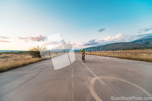 Image of Triathlete riding his bicycle during sunset, preparing for a marathon. The warm colors of the sky provide a beautiful backdrop for his determined and focused effort.