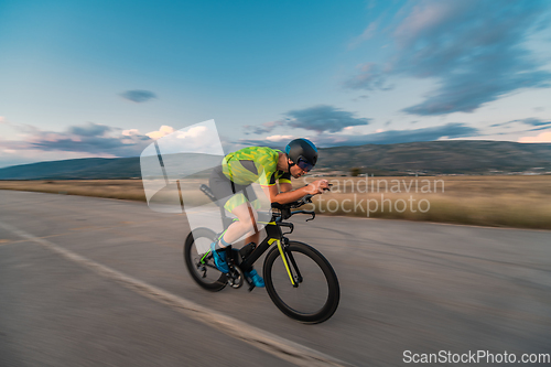 Image of Triathlete riding his bicycle during sunset, preparing for a marathon. The warm colors of the sky provide a beautiful backdrop for his determined and focused effort.