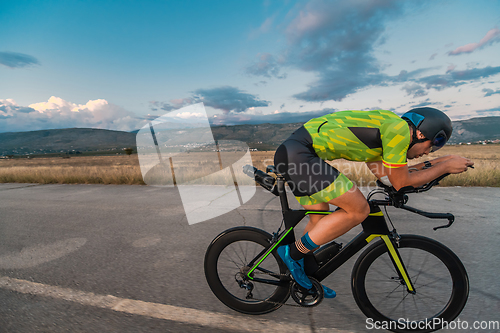 Image of Triathlete riding his bicycle during sunset, preparing for a marathon. The warm colors of the sky provide a beautiful backdrop for his determined and focused effort.