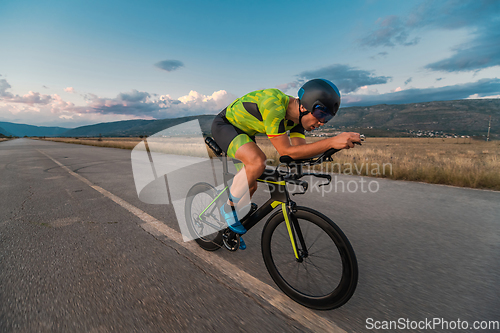 Image of Triathlete riding his bicycle during sunset, preparing for a marathon. The warm colors of the sky provide a beautiful backdrop for his determined and focused effort.