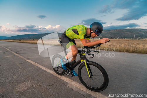 Image of Triathlete riding his bicycle during sunset, preparing for a marathon. The warm colors of the sky provide a beautiful backdrop for his determined and focused effort.