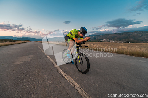 Image of Triathlete riding his bicycle during sunset, preparing for a marathon. The warm colors of the sky provide a beautiful backdrop for his determined and focused effort.