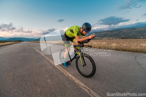 Image of Triathlete riding his bicycle during sunset, preparing for a marathon. The warm colors of the sky provide a beautiful backdrop for his determined and focused effort.