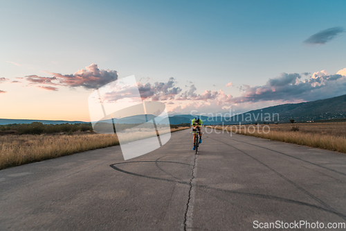 Image of Triathlete riding his bicycle during sunset, preparing for a marathon. The warm colors of the sky provide a beautiful backdrop for his determined and focused effort.