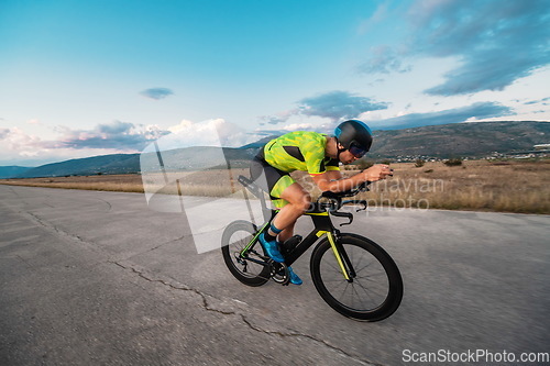 Image of Triathlete riding his bicycle during sunset, preparing for a marathon. The warm colors of the sky provide a beautiful backdrop for his determined and focused effort.