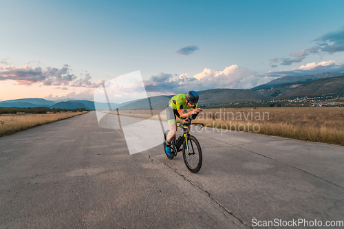 Image of Triathlete riding his bicycle during sunset, preparing for a marathon. The warm colors of the sky provide a beautiful backdrop for his determined and focused effort.