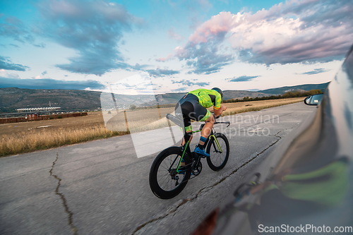 Image of Triathlete riding his bicycle during sunset, preparing for a marathon. The warm colors of the sky provide a beautiful backdrop for his determined and focused effort.