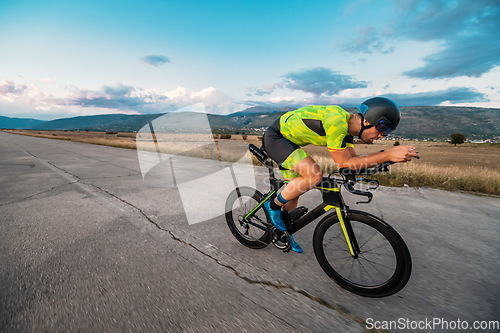 Image of Triathlete riding his bicycle during sunset, preparing for a marathon. The warm colors of the sky provide a beautiful backdrop for his determined and focused effort.