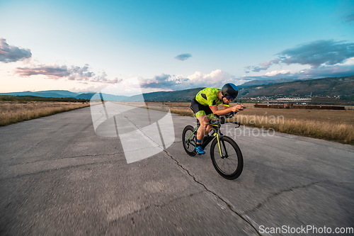 Image of Triathlete riding his bicycle during sunset, preparing for a marathon. The warm colors of the sky provide a beautiful backdrop for his determined and focused effort.