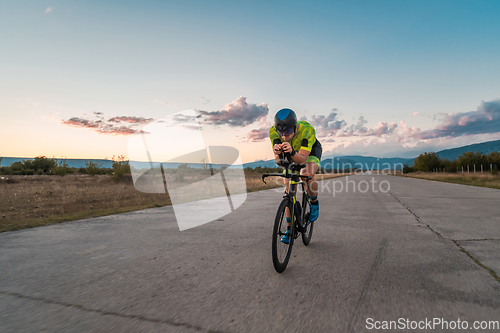 Image of Triathlete riding his bicycle during sunset, preparing for a marathon. The warm colors of the sky provide a beautiful backdrop for his determined and focused effort.