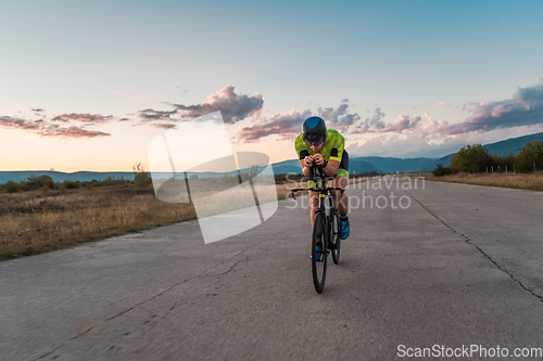 Image of Triathlete riding his bicycle during sunset, preparing for a marathon. The warm colors of the sky provide a beautiful backdrop for his determined and focused effort.