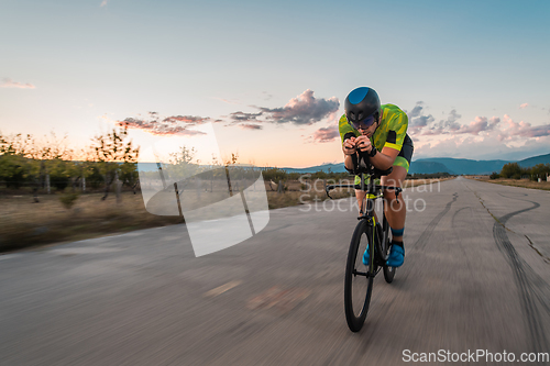 Image of Triathlete riding his bicycle during sunset, preparing for a marathon. The warm colors of the sky provide a beautiful backdrop for his determined and focused effort.