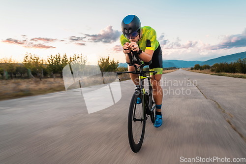 Image of Triathlete riding his bicycle during sunset, preparing for a marathon. The warm colors of the sky provide a beautiful backdrop for his determined and focused effort.