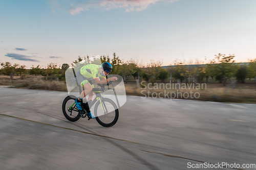 Image of Triathlete riding his bicycle during sunset, preparing for a marathon. The warm colors of the sky provide a beautiful backdrop for his determined and focused effort.