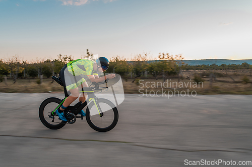 Image of Triathlete riding his bicycle during sunset, preparing for a marathon. The warm colors of the sky provide a beautiful backdrop for his determined and focused effort.