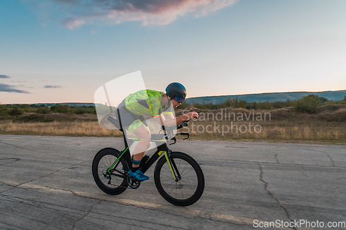 Image of Triathlete riding his bicycle during sunset, preparing for a marathon. The warm colors of the sky provide a beautiful backdrop for his determined and focused effort.