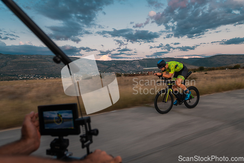 Image of A videographer recording a triathlete riding his bike preparing for an upcoming marathon.Athlete's physical endurance and the dedication required to succeed in the sport.