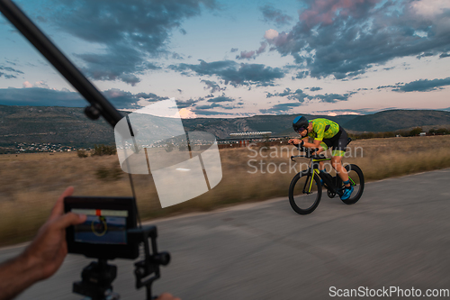 Image of A videographer recording a triathlete riding his bike preparing for an upcoming marathon.Athlete's physical endurance and the dedication required to succeed in the sport.