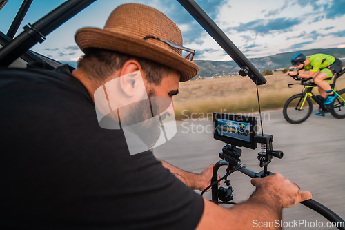 Image of A videographer recording a triathlete riding his bike preparing for an upcoming marathon.Athlete's physical endurance and the dedication required to succeed in the sport.