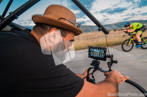 Image of A videographer recording a triathlete riding his bike preparing for an upcoming marathon.Athlete's physical endurance and the dedication required to succeed in the sport.