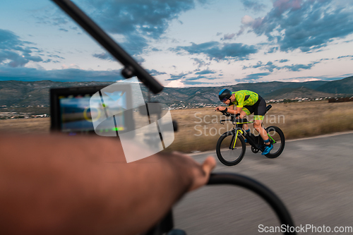 Image of A videographer recording a triathlete riding his bike preparing for an upcoming marathon.Athlete's physical endurance and the dedication required to succeed in the sport.