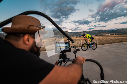 Image of A videographer recording a triathlete riding his bike preparing for an upcoming marathon.Athlete's physical endurance and the dedication required to succeed in the sport.