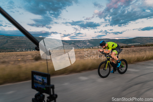 Image of A videographer recording a triathlete riding his bike preparing for an upcoming marathon.Athlete's physical endurance and the dedication required to succeed in the sport.