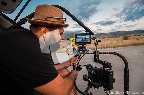 Image of A videographer recording a triathlete riding his bike preparing for an upcoming marathon.Athlete's physical endurance and the dedication required to succeed in the sport.