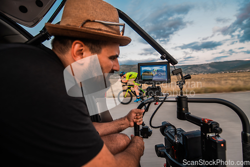 Image of A videographer recording a triathlete riding his bike preparing for an upcoming marathon.Athlete's physical endurance and the dedication required to succeed in the sport.