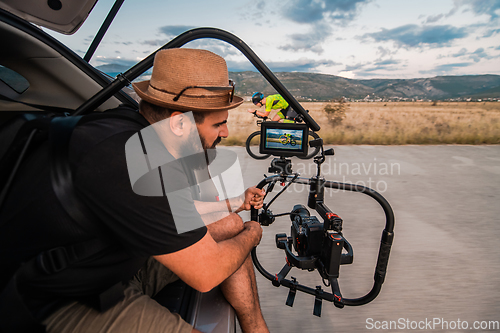 Image of A videographer recording a triathlete riding his bike preparing for an upcoming marathon.Athlete's physical endurance and the dedication required to succeed in the sport.