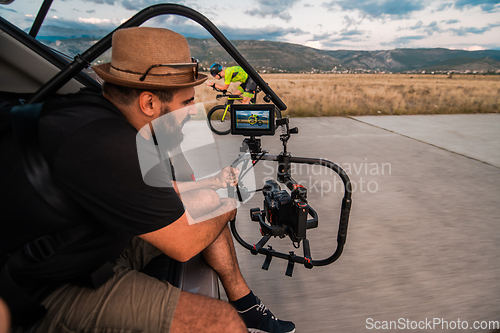 Image of A videographer recording a triathlete riding his bike preparing for an upcoming marathon.Athlete's physical endurance and the dedication required to succeed in the sport.