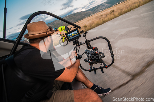Image of A videographer recording a triathlete riding his bike preparing for an upcoming marathon.Athlete's physical endurance and the dedication required to succeed in the sport.
