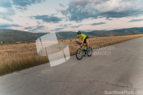 Image of Triathlete riding his bicycle during sunset, preparing for a marathon. The warm colors of the sky provide a beautiful backdrop for his determined and focused effort.